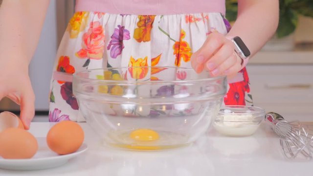 Woman cracking eggs into a glass bowl. Closeup of a pair of hands cracking an egg for cooking. Cook tasty food at home. Girl in a beautiful apron. 