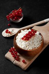 homemade cottage cheese with currants in a wooden plate against a dark background, a healthy milk breakfast with berries on a black table