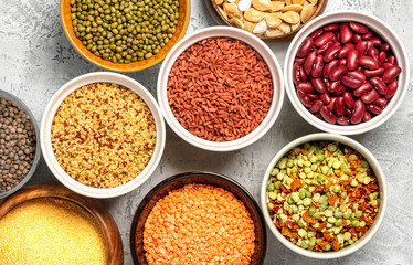 Various cereals and legumes. Beans, peas, lentils, mung bean, polenta and bulgur in bowls on a gray concrete background, top view. Protein foods for vegans and vegetarians.