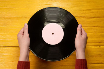 Vinyl record in female hand on yellow wooden flat lay background.