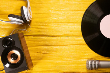 Vinyl record, microphone, headphones and loudspeaker on yellow flat lay background with copy space.