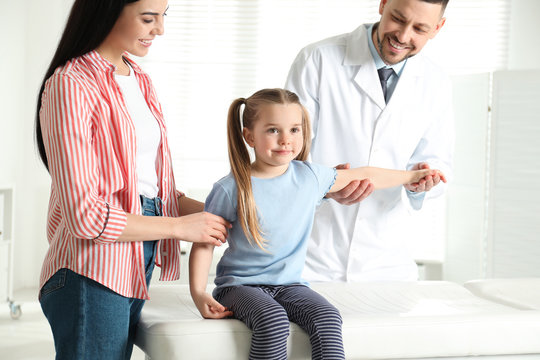 Professional orthopedist examining little patient's arm in clinic