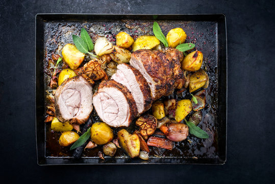 Traditional roasted veal roll roast offered with potatoes, carrots and onions as top view on a metal sheet with copy space