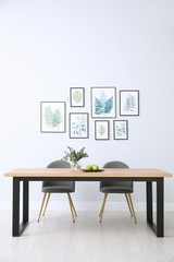 Stylish room interior with modern table, chairs and paintings of tropical leaves. Idea for design
