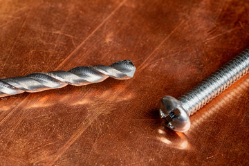 A  used and worn drill bit and a screw waiting to be used again, resting on a worn and oxidized copper work surface.  Shot for Copy writing with plenty of negative space.