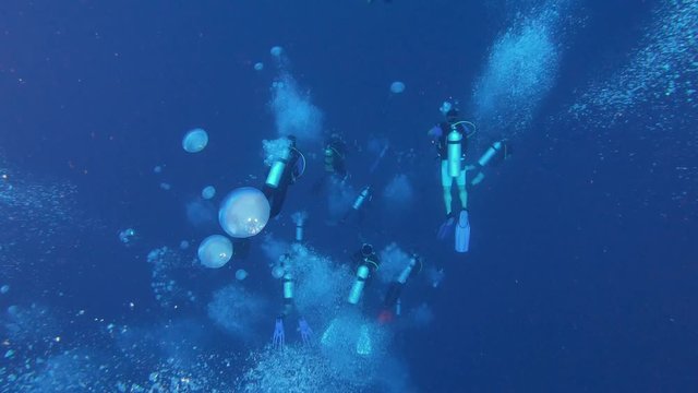 Scuba divers going deep in dark blue water 