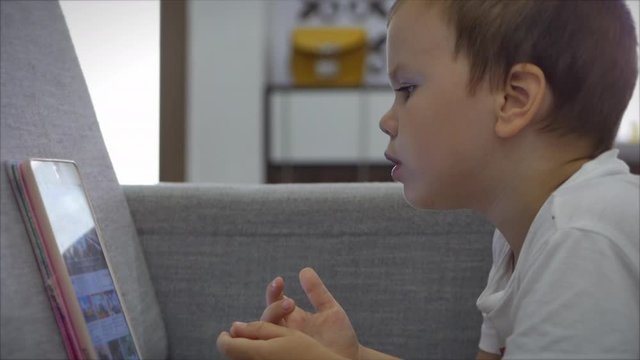 Curious cute preschool kid girl using digital tablet technology device lying on carpet floor alone. Small child hold pad computer surfing internet play game at home. Children tech addiction concept