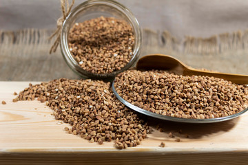 On a board is a plate with buckwheat. On top is a wooden spoon. Buckwheat woke from a can on a board.