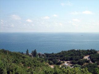 Sea view from the coastal mountains. The coastal hills are surrounded by dense vegetation, including low buildings. In the distance, on the horizon, you can see the coastal mountains in the haze.