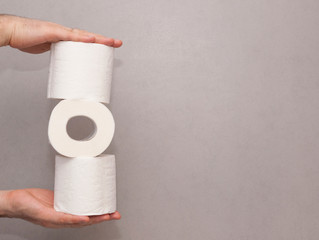 Male hands holding a tower made of three white toilet paper rolls against the gray wall in bathroom