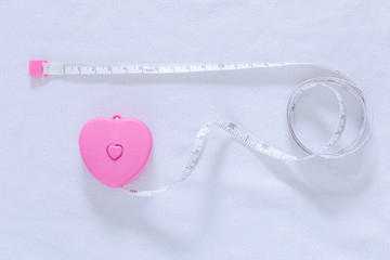 A measuring tape shaping a heart,Pink hearts with meters around on a white background