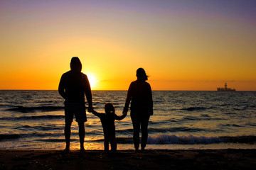 A silhouette of a young family looking out to sea in the sunset or sunrise.