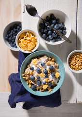 Bowl with oatmeal, cornflakes and blueberries on a white wooden background.