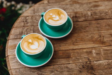 Round wooden table with two blue ceramic cups of tasty hot coffee with heart-shaped drawing made of milk foam. Aroma beverage freshly brewed in the morning to awake.