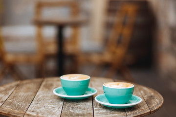 Freshly brewed coffee in turquoise-coloured cups with latte art on wooden table with blur background of cafe terrace. Start your day with tasty hot beverage