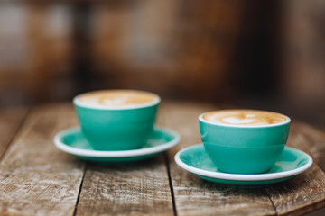 Light blue cups of hot fresh coffee with heart-shaped drawing made of milk foam on dark wooden table with blur background. Aroma drink brewed in the morning to awake
