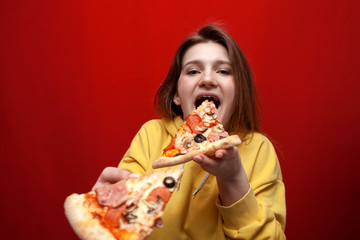young happy girl eating pizza on a colored background, a teenager holds two slices of pizza and eat fast food