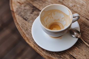 Cappuccino coffee stain in almost empty white cup with milk foam on walls on wooden table with blur background. Frothy coffee in ceramic cup