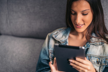 Smiling teenage woman looking at social networks and studying in a tablet at home. Stay at home and spend time for you.