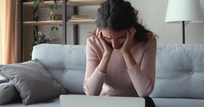 Worried young adult woman looking at laptop feeling frustrated desperate reading bad negative online news sitting at home. Stressed upset female user using computer anxious about financial problems.