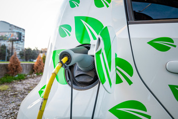 Small electric car with leafs on the side being charged up on a street.