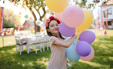 Small girl outdoors in garden in summer, playing with balloons.