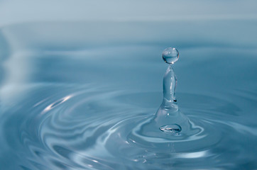 water drop art. water droplet splashes into the water and creates ripple. azure colored water and reflections.