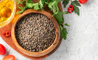 Uncooked dry green french lentils in a wooden bowl on concrete background top view.