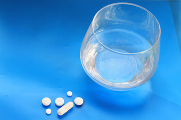  white pills and a glass of water stands on a table on a blue background