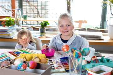 Portrait of adorable blonde girl at home painting easter eggs