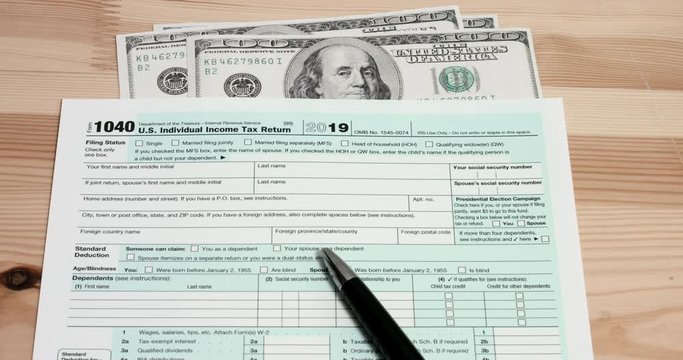 Pen falling on US 1040 tax day return form with 100 usd dollar bills.
