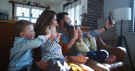 Happy young Caucasian family with three kids wave to friends talking during smartphone video call at home slow motion.