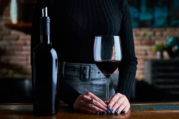  Woman in black shirt and grey skirt tasting red wine. Close up image of woman holding wine glass and wine bottle. © a.dl
