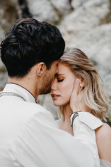 noise effect, selective focus: incredibly enamored brides hugging, kissing and posing for a photo on the incredible rocky mountains background with a big waterfall