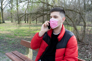 Coronavirus protection. man in medical protective mask is sitting with a smartphone on city street in Europe. tourists on street wear protective mask from viruses. concept health and safety