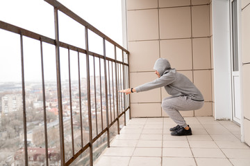 Athletic man in training clothes performs an exercise on the legs squat on the balcony of his...
