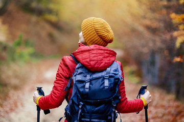 Hiking girl with poles and backpack on a trail. Backview. Travel and healthy lifestyle outdoors in fall season.