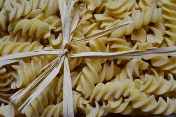 Close-up, background and texture of raw spiral pasta wrapped in a bast bow