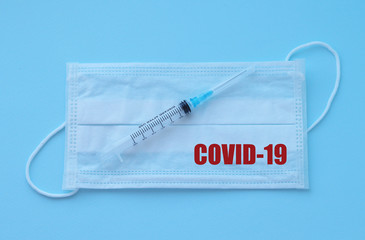 A medical syringe lies on a protective mask with the inscription: "covid-19" on a blue background. Selective focus. Coronavirus 