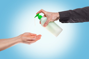 A man's hand drips antibacterial soap for disinfection on women's palms. Light blue background. Copy space. Concept of a viral pandemic, protection from bacteria and health