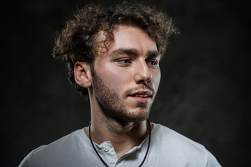 Close-up portrait of a young handsome male model posing on a grey background in a dark studio,...