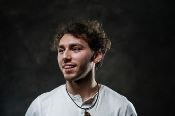 Curly and hansome caucasian man standing in a dark studio on a grey background, wearing casual white shirt looking interested