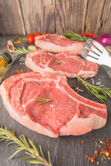 Three raw steaks with bone on a black slate, with spices, food style, close-up