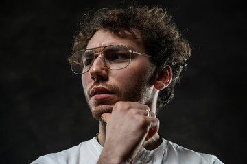 Close-up portrait of a young handsome male model posing on a grey background in a dark studio,...