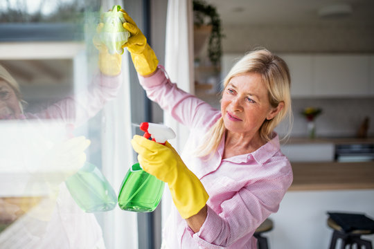Portrait of senior woman cleaning windows indoors at home.