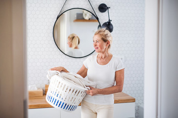 Portrait of senior woman with laundry basket indoors at home.