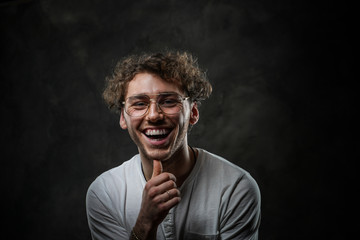 Portrait of a smiling young adult guy, wearing casual white shirt and sunglasses. Making a gesture...