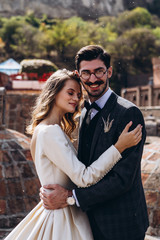 wedding photoshoot of attractive couple in Georgia: perfect appearance, stylish wedding clothes, bouquet, decor, spectacular locations of the old city of Tbilisi