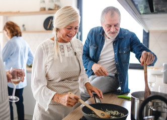 Group of senior friends at dinner party at home, cooking.