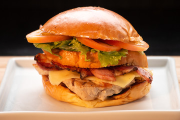Sanduíche de filé de frango com salada de alface e tomate e bacon com queijo em prato branco de louça em fundo preto
